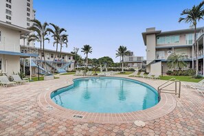 A swimming pool surrounded by hexagonal tiles, with lounge chairs and palm trees.