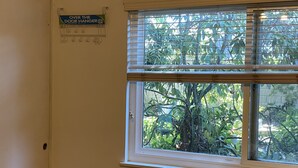 Ett rum med ett fönster som vetter mot en trädgård, en dörr med en hängande skylt och en väggmonterad ljusströmbrytare.