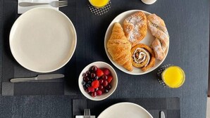 Een ontbijt met croissants, bessen en twee glazen sinaasappelsap op een donkere tafel.