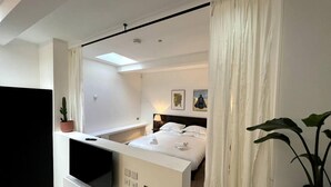 Een moderne hotelkamer met een bed, een televisie, een kamerplant en een raam met gordijnen.