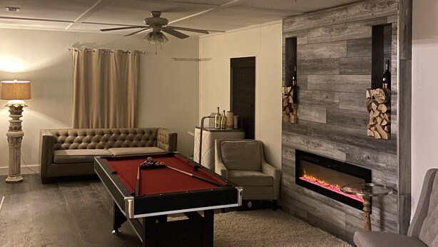 A modern living room with a pool table, a fireplace, a sofa, and a ceiling fan. - Hollywood Island (Indianapolis)