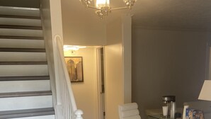 A staircase with white balusters, a white chair, a glass table with a lamp, and a framed picture on the wall. - Hollywood Island (Indianapolis)