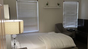 A bedroom with a bed, a desk, a chair, and two windows with blinds. - Hollywood Island (Indianapolis)
