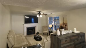 A living room with a fireplace, a sofa, a coffee table, a TV, and a decorative Eiffel Tower painting. - Hollywood Island (Indianapolis)