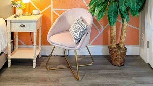 A room with a geometric-patterned wall, a white bedside table with a lamp, a chair with a patterned cushion, and a potted plant. - Central 1BDR+PetsOK+Extended Stay Discounts (Corpus Christi)