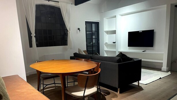 Ein modernes Wohnzimmer mit einem runden Holztisch, einer Couch und einem an der Wand befestigten Fernseher.