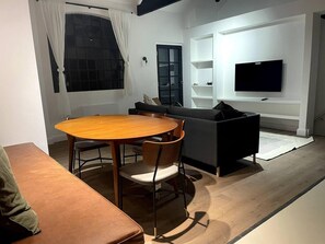A modern living room with a round wooden table, a sofa, and a television mounted on the wall. - Design led Duplex Apartment in Buzzing Queens Park (London)