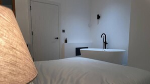 Ein Schlafzimmer mit einem Bett, einer weißen Tür, einem wandmontierten Waschbecken und einem Handtuchspender.