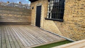 Eine Holzterrasse mit einer Ziegelwand und einem Fenster.