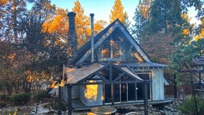 Une cabane avec une cheminée en pierre, un patio couvert avec des chaises et un sentier en pierre.