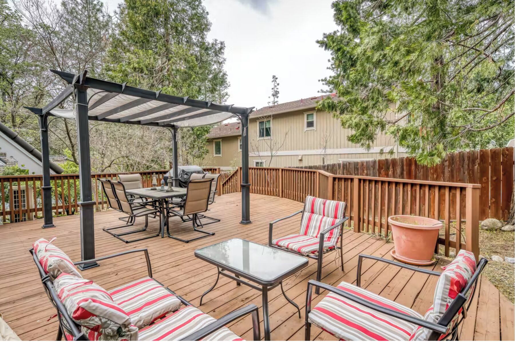 A covered deck with a pergola, outdoor furniture, and a large potted plant.