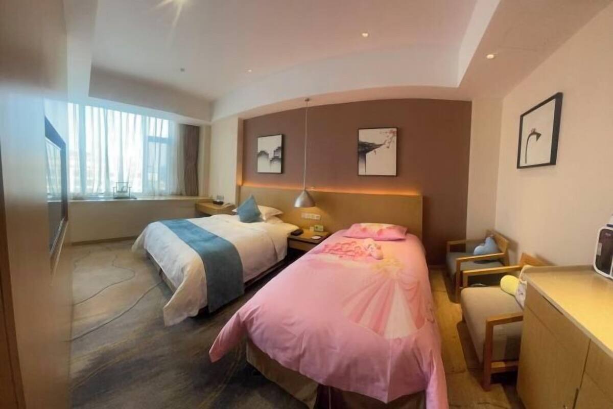 Quarto de hotel com duas camas, uma escrivaninha e uma janela com cortinas.