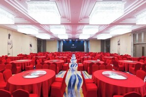 A conference room with rows of round tables and chairs, a stage at the front, and a large screen. - Canal Hotel (Jiaxing)