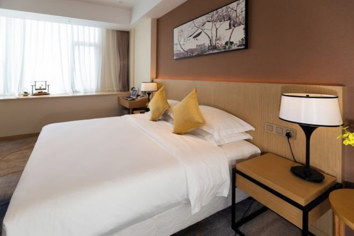 A hotel room with a large bed, bedside tables, a lamp, a painting on the wall, and a window with curtains.