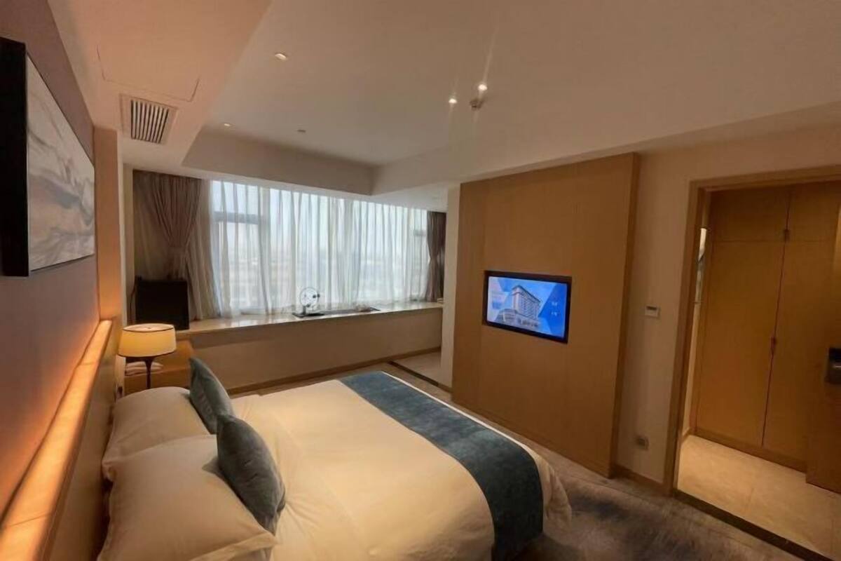 Quarto de hotel com cama, televisão, janela com cortinas e porta.