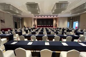A conference room with rows of tables, chairs, and a stage. - Canal Hotel (Jiaxing)