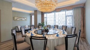 A round dining table with chairs, a chandelier, and a sofa in a room with large windows and a patterned wall. - Canal Hotel (Jiaxing)