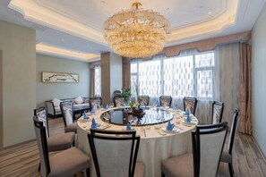 A round dining table with chairs, a chandelier, and a sofa in a room with large windows and a patterned wall. - Canal Hotel (Jiaxing)