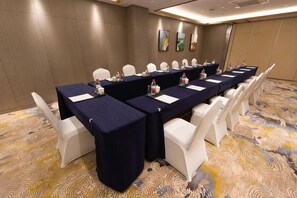 Una sala de conferencias con una larga mesa, sillas blancas y una alfombra estampada.
