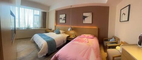 A hotel room with two beds, a desk, a chair, and a TV.