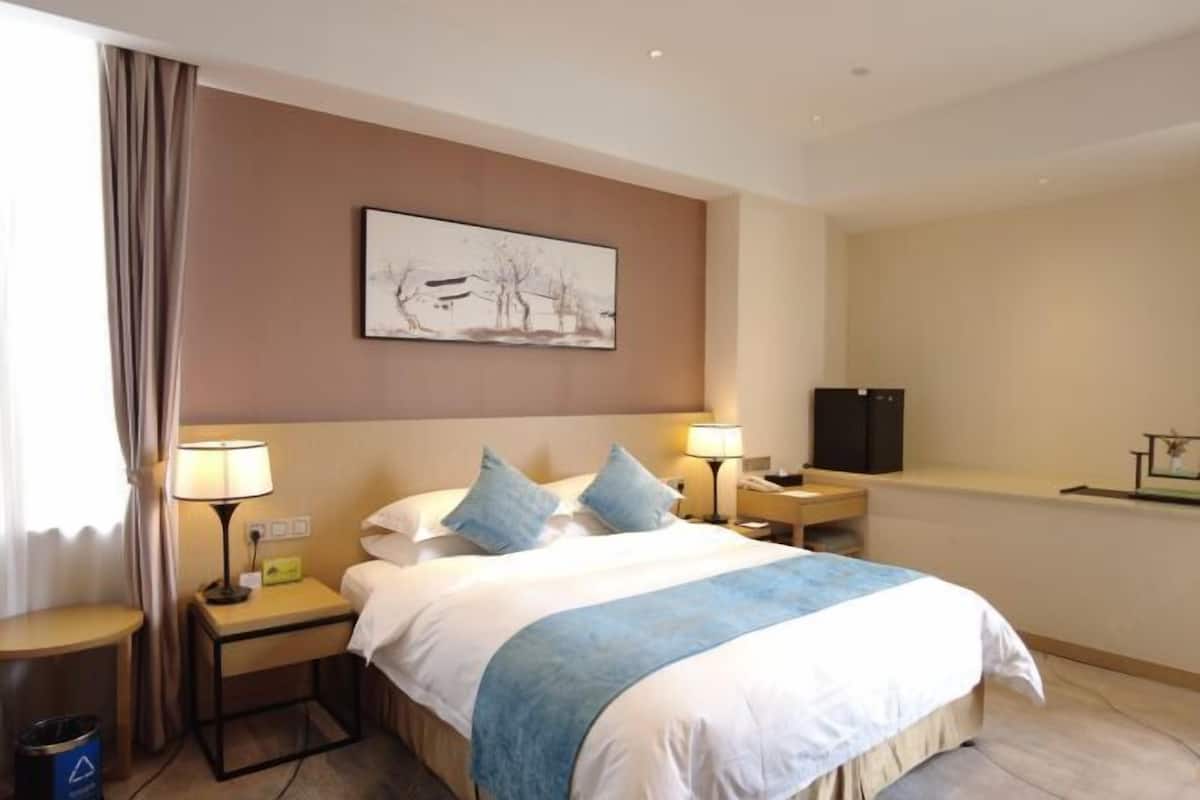 Quarto de hotel com cama, abajures, TV de tela plana, pintura na parede e janela com cortinas.