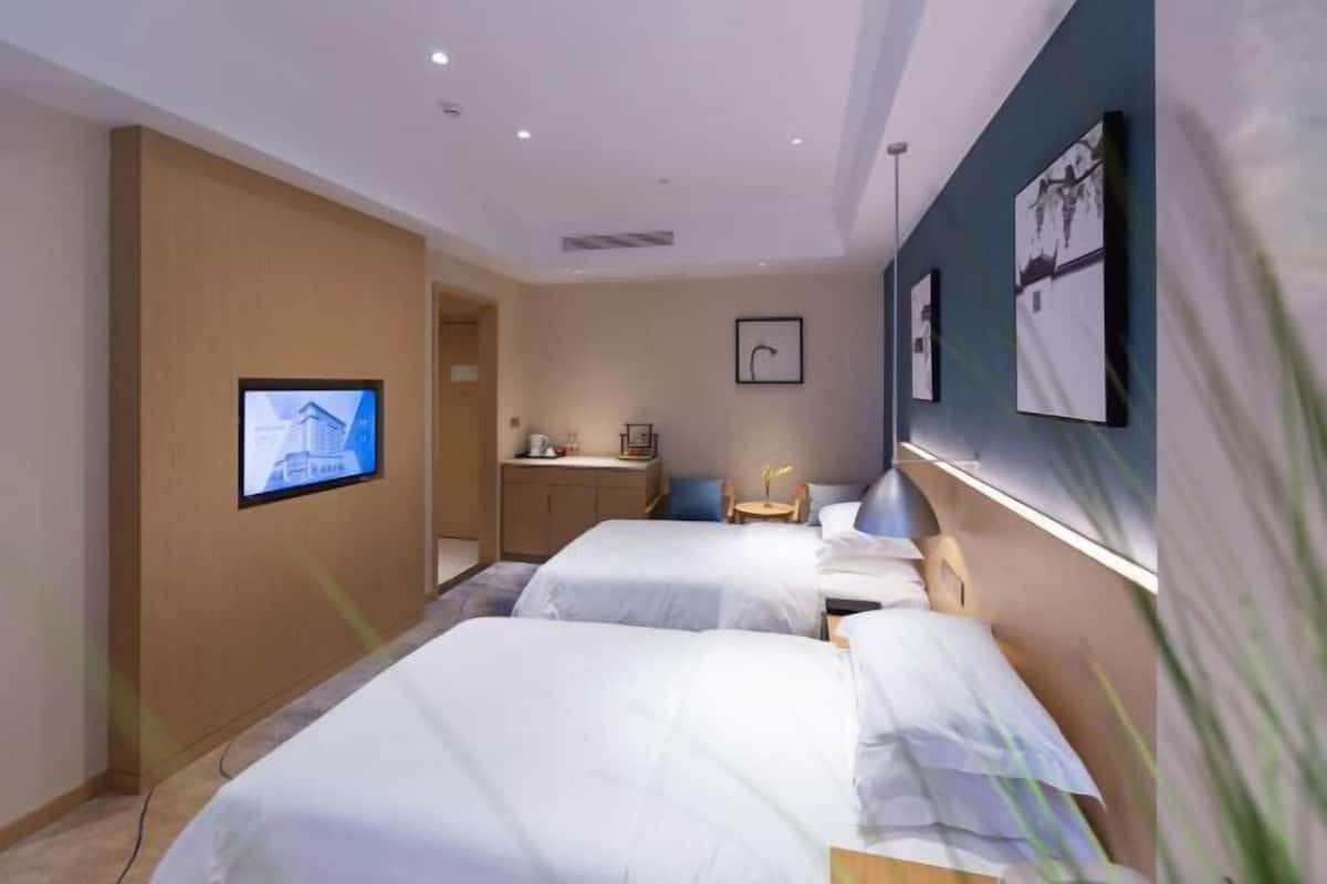 Quarto de hotel com duas camas, uma escrivaninha, uma cadeira e uma TV fixada na parede.