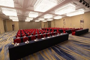 A conference room with rows of red chairs, a long table, and chandeliers. - Canal Hotel (Jiaxing)