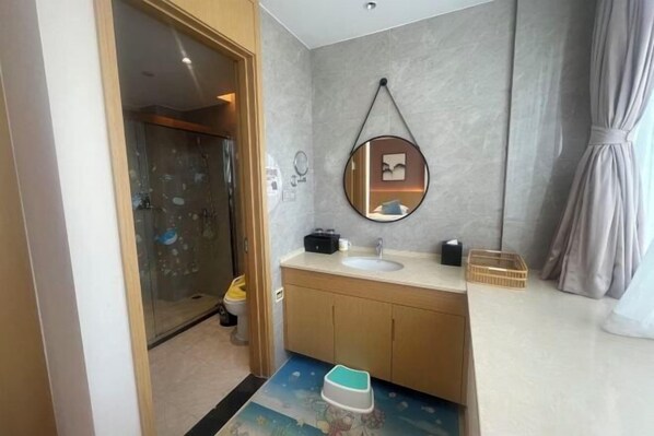 A modern bathroom with a glass shower, a wooden vanity, a round mirror, and a small sink. - Canal Hotel (Jiaxing)