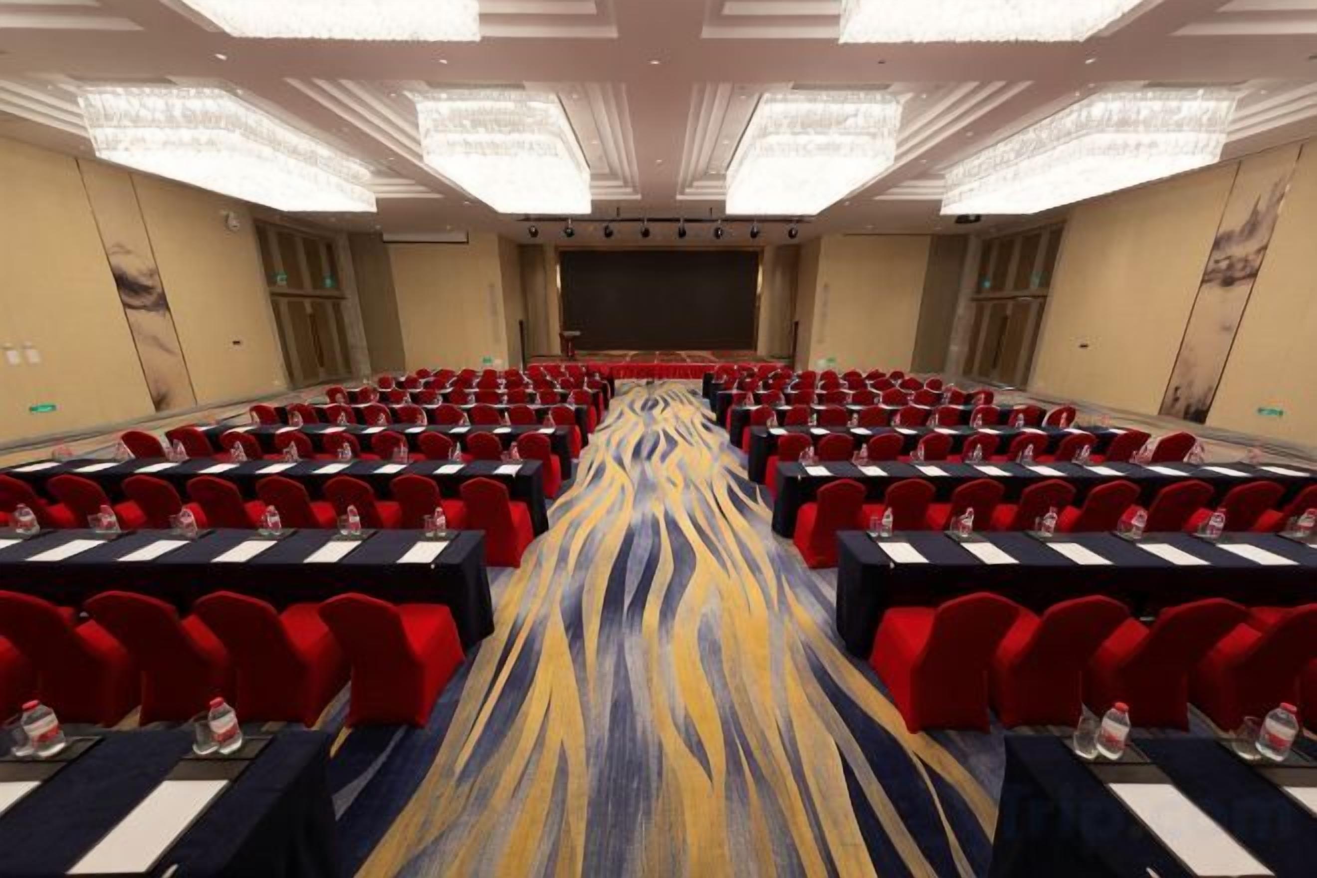 A conference room with rows of tables and chairs, a stage, and a carpeted floor.