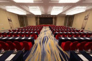 A conference room with rows of tables and chairs, a stage, and a carpeted floor. - Canal Hotel (Jiaxing)