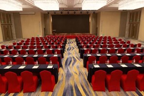 A conference room with rows of tables and chairs, a stage, and a large screen. - Canal Hotel (Jiaxing)