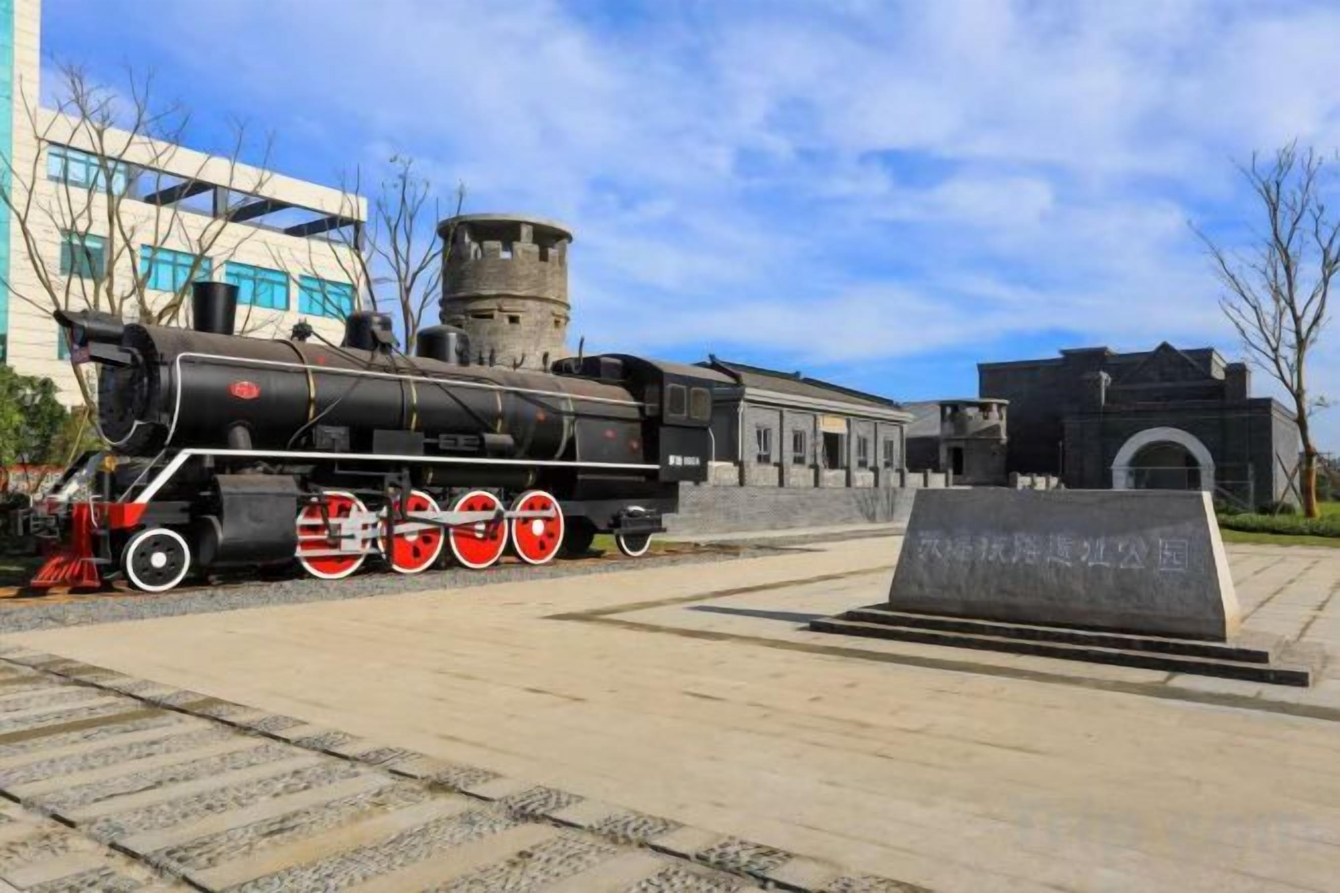 Eine ausgestelltе Dampflokomotive mit einer Schautafel vor dem Hintergrund moderner Gebäude und eines klaren Himmels.
