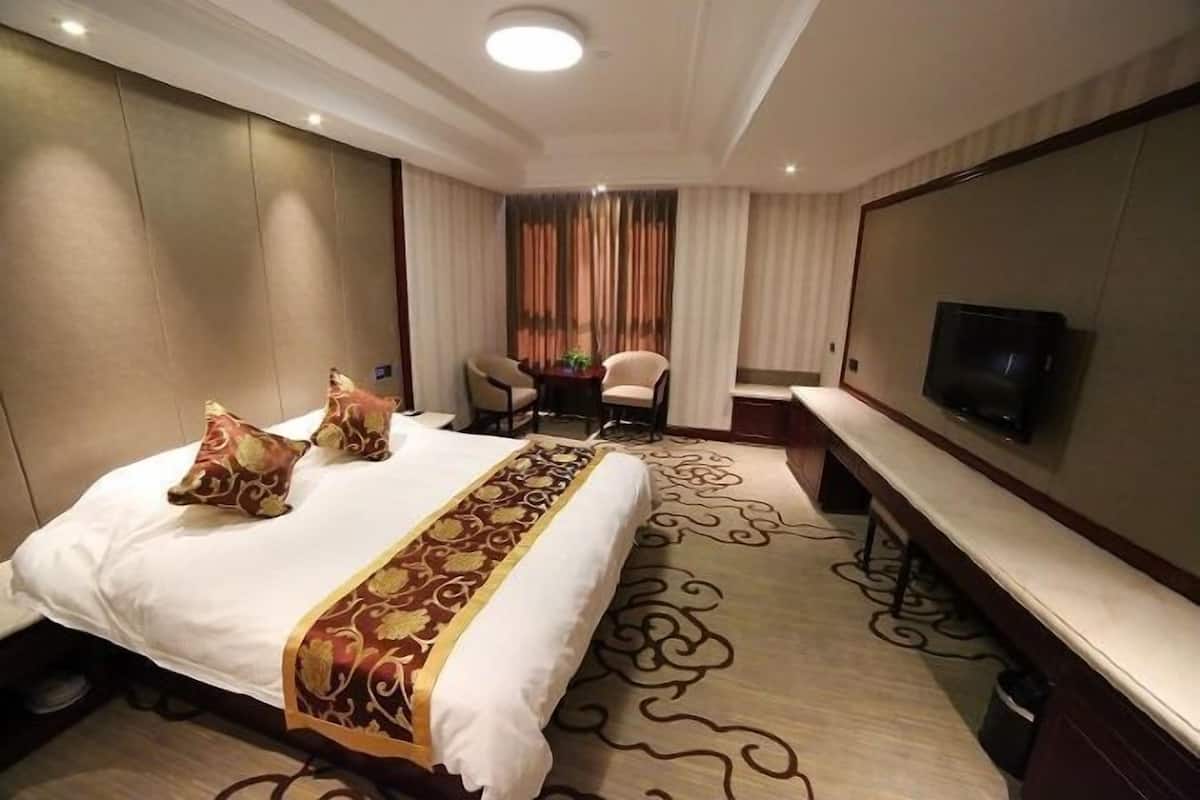 A hotel room with a large bed, a TV, a desk, and a chair.