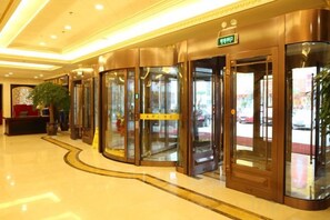 A hotel lobby with revolving doors, a reception desk, and a potted plant. - Taihua Hotel (Rugao)