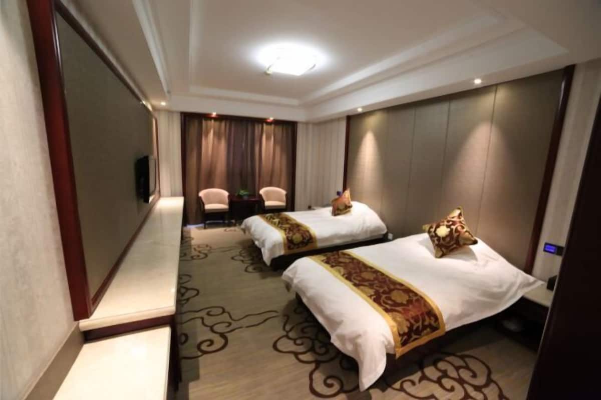A hotel room with two beds, a TV, a desk, and a chair.