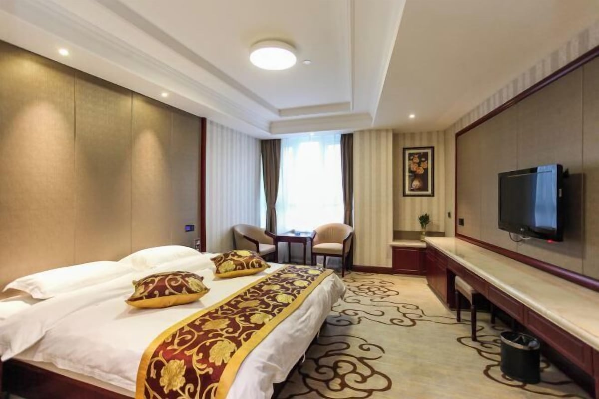 A hotel room with a bed, a desk, a television, and a window with curtains.