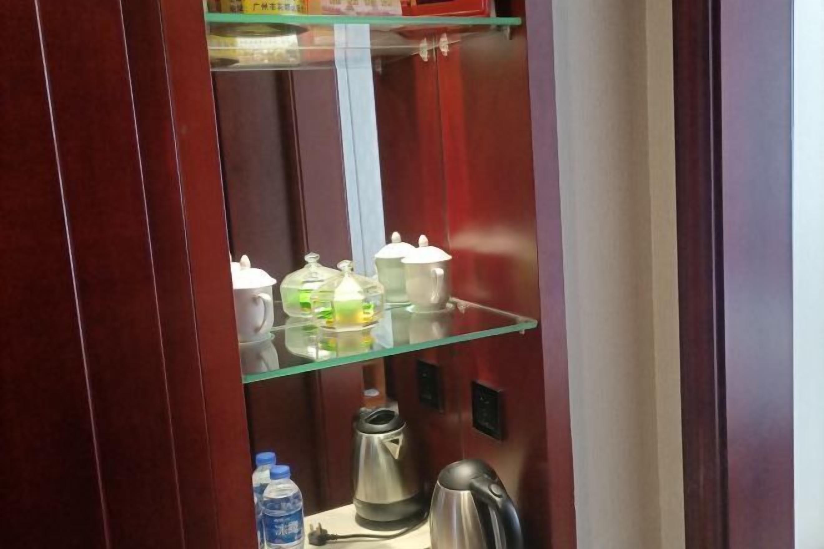 Habitación de hotel con repisa de vidrio que sostiene varios objetos, una tetera y una botella de agua.