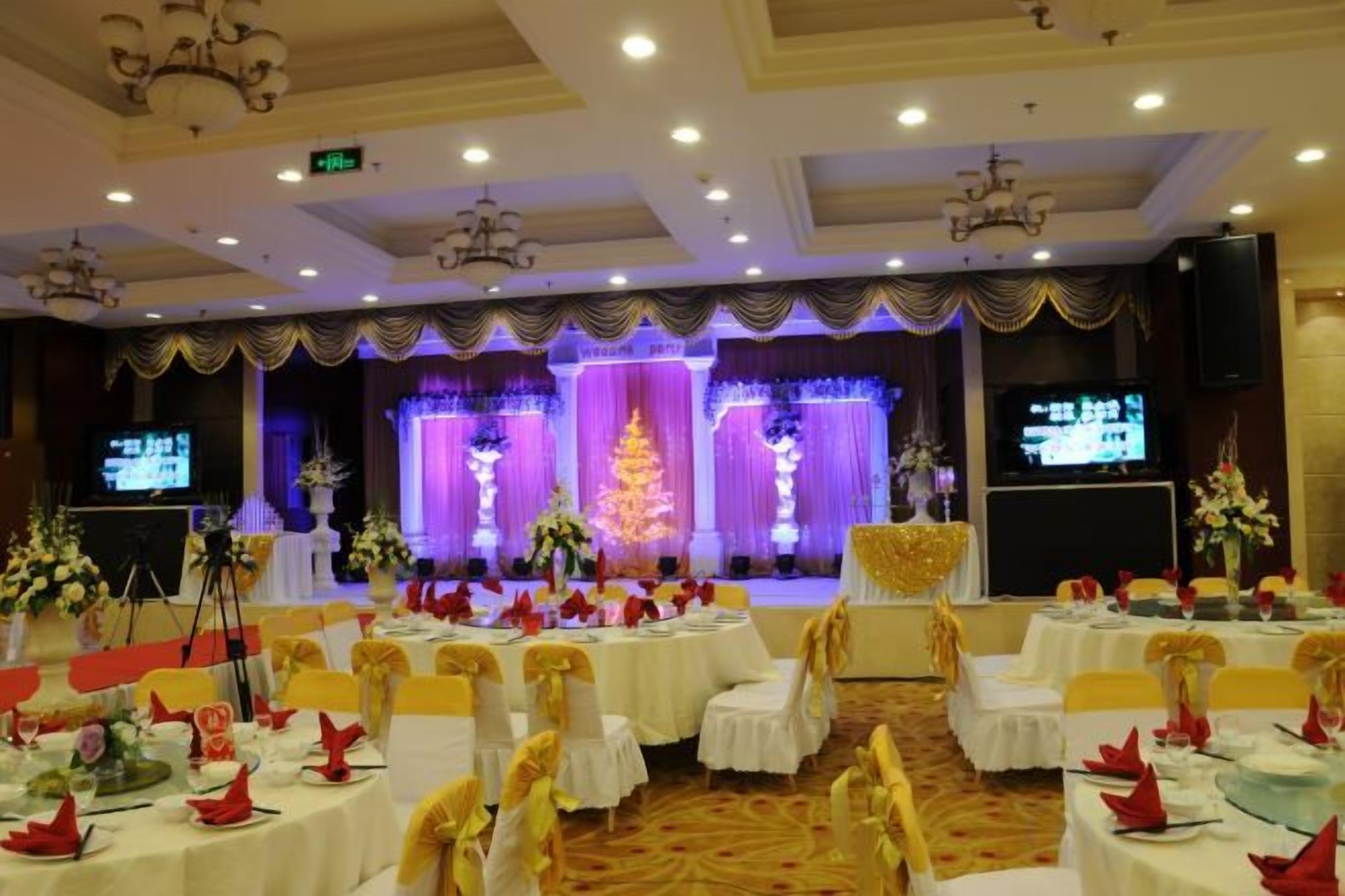 A banquet hall with round tables, chairs, and a stage with a Christmas tree.