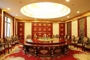 A conference room with a large round table surrounded by chairs, ornate wall panels, and a patterned carpet. - Taihua Hotel (Rugao)