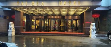 La entrada del Hotel Tai Hua, con alfombra roja, puertas dobles y una estatua a cada lado.