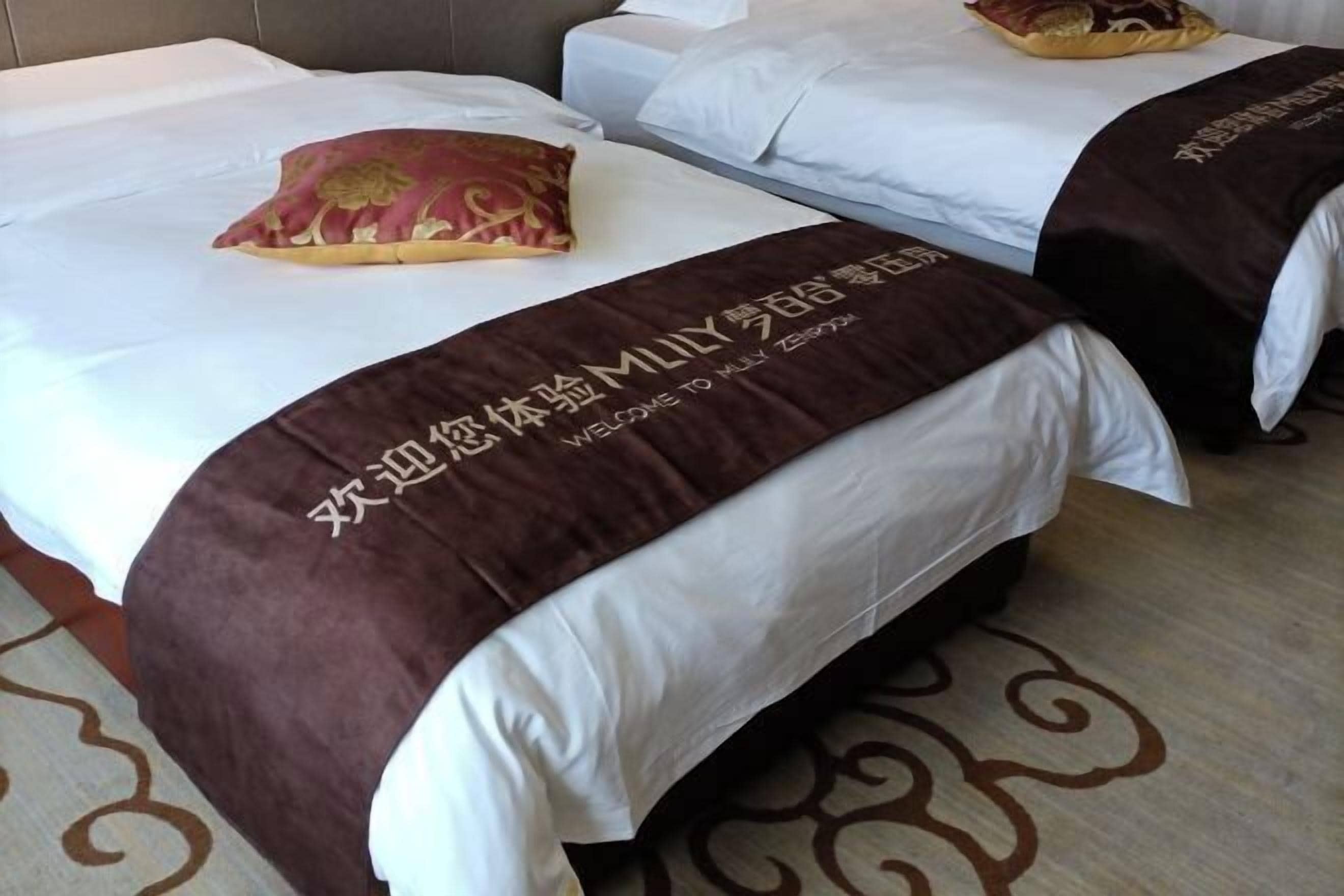 Une chambre d’hôtel avec deux lits, chacun recouvert d’une couverture marron et agrémenté d’un oreiller à motifs floraux. La chambre est dotée d’une moquette à motifs et d’une tête de lit.