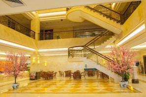 Um saguão de hotel com piso xadrez, escada e plantas em vasos.