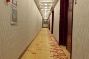 Un couloir d'hôtel avec un sol recouvert de moquette, des portes de chaque côté et un plafond doté d'un éclairage encastré.