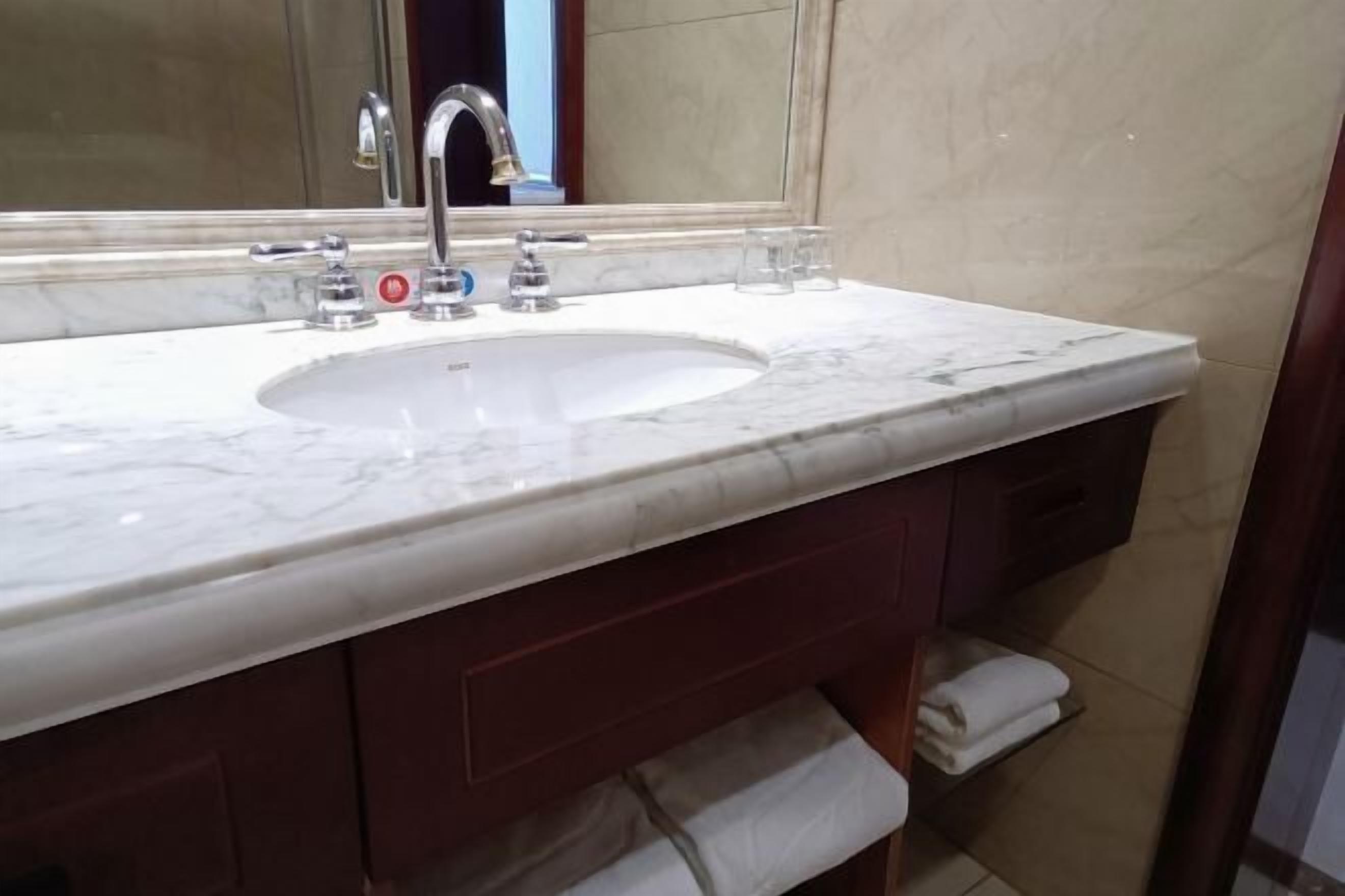 A bathroom with a marble sink, a mirror, and a towel rack.