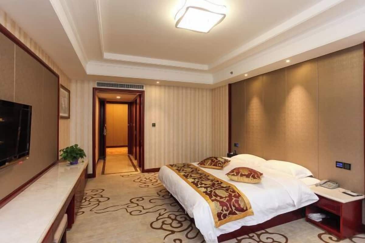 A hotel room with a bed, a desk, a TV, and a door leading to another room.