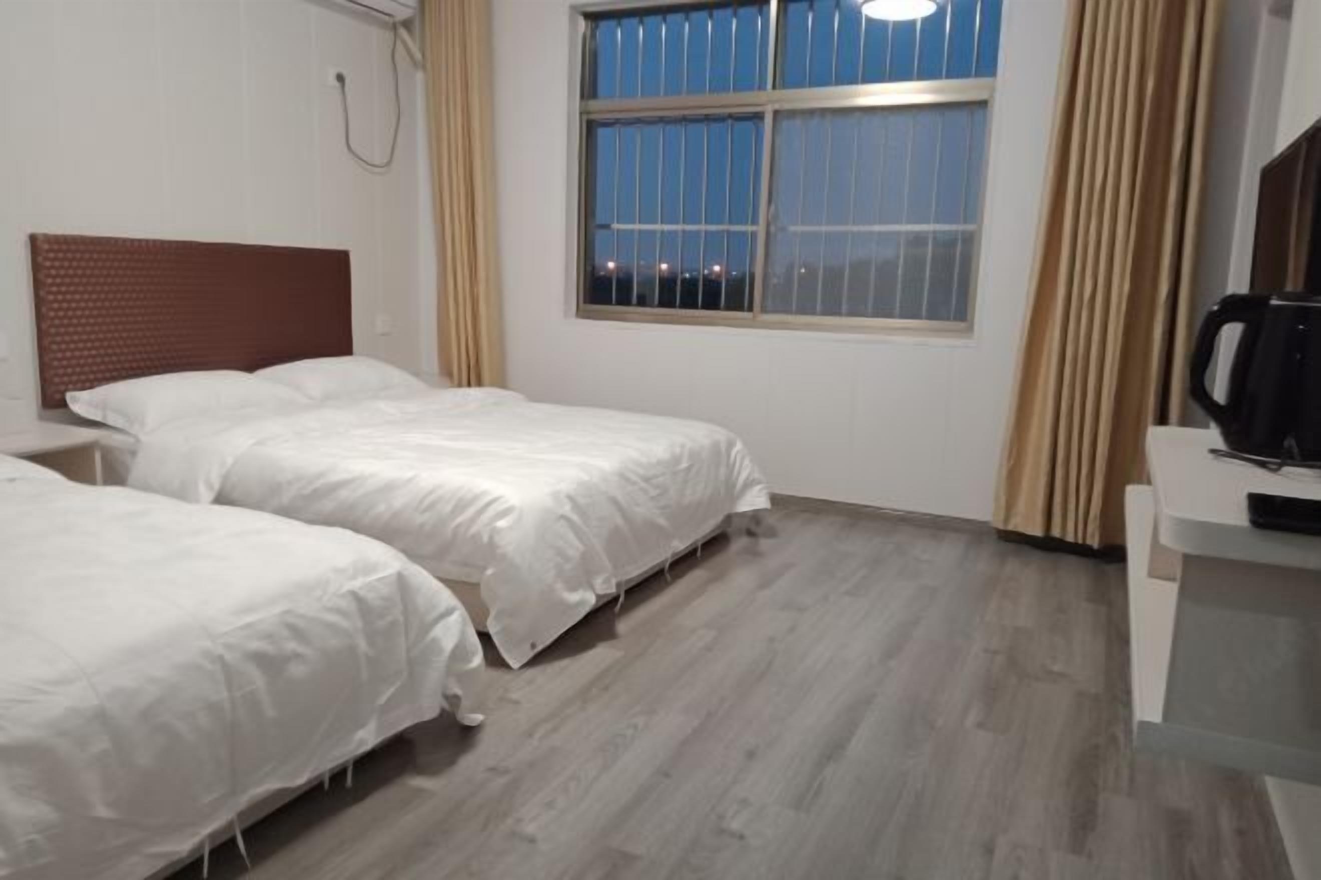 Habitación de hotel con dos camas individuales, una ventana con vistas a la ciudad de noche, suelo de madera y un escritorio pequeño con cafetera.