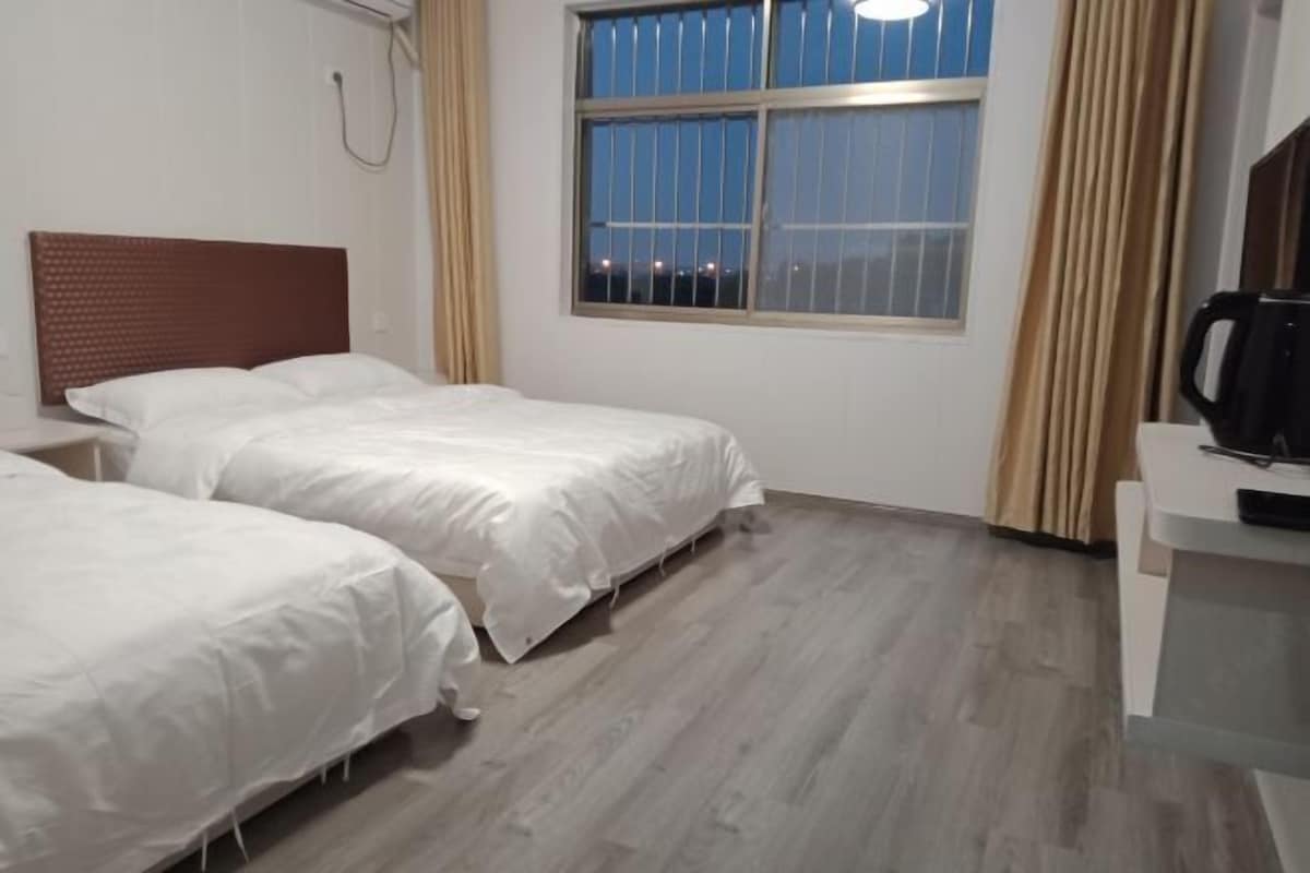 Hotellihuone, jossa on kaksi erillistä sänkyä, ikkuna, josta avautuu näkymä kaupunkiin yöllä, puulattia ja pieni työpöytä, jossa on kahvinkeitin.