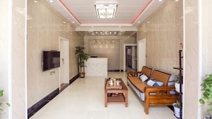 A hotel lobby with a sofa, a TV, a plant, and a reception desk.