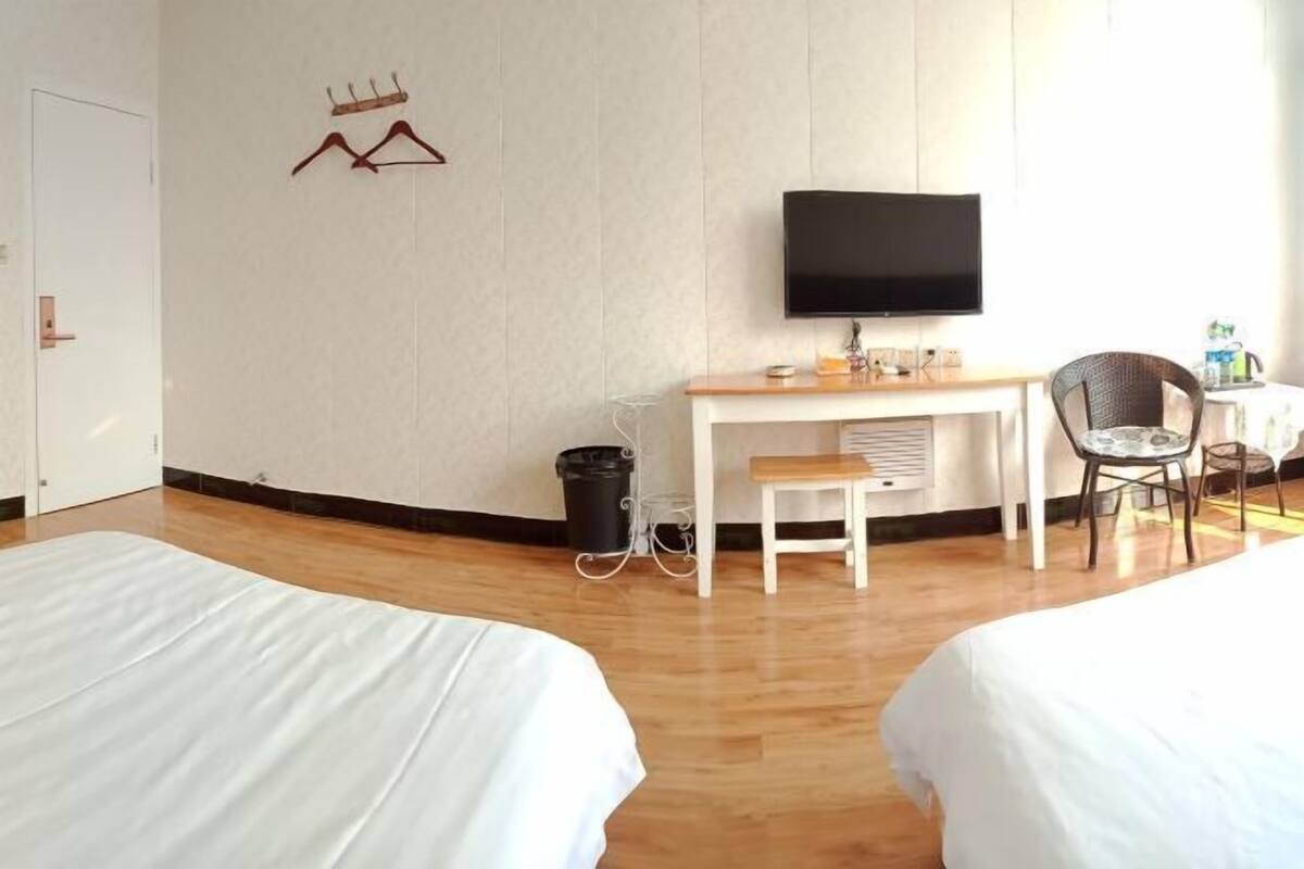 A hotel room with two beds, a desk, a chair, a TV, and a wall-mounted coat rack.