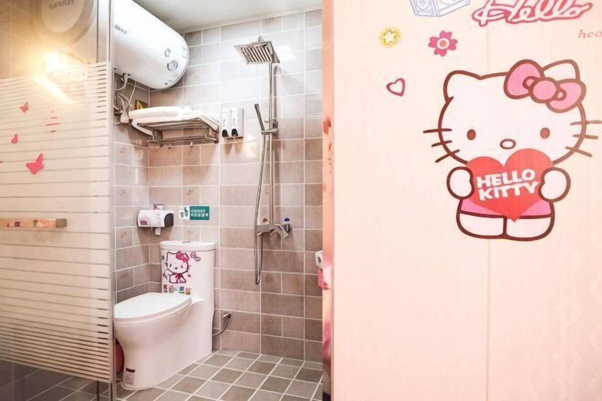 A bathroom with a toilet, shower, and a Hello Kitty wall decal.